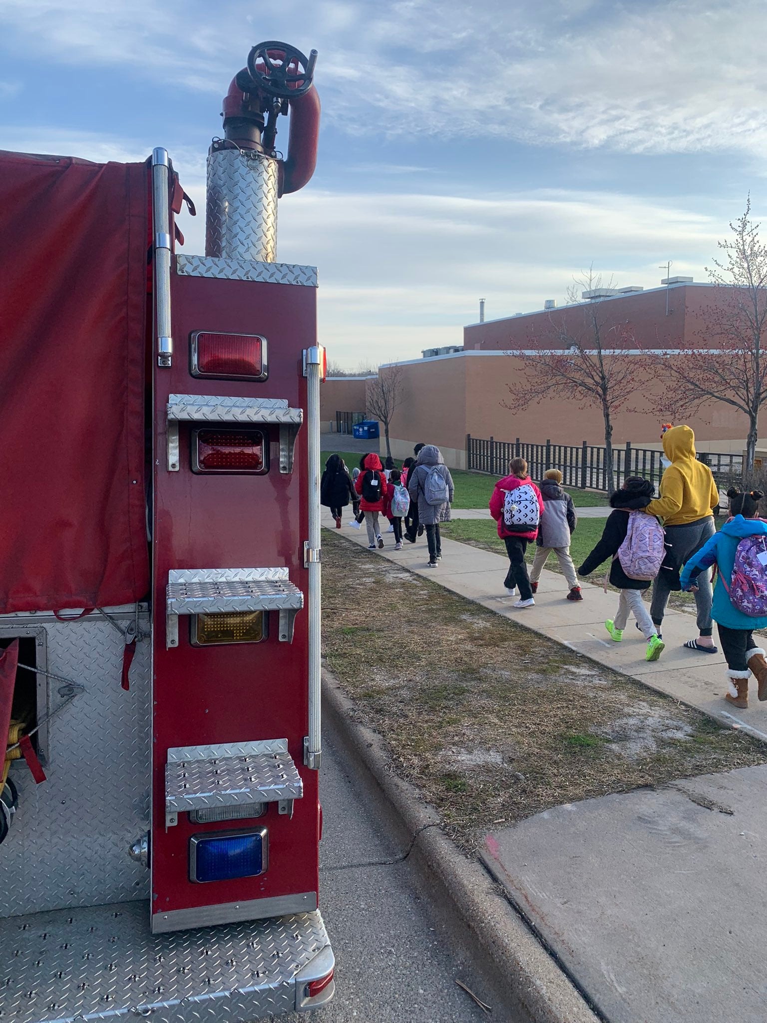 Students walk on the sidewalk alongside a red fire truck in Saint Paul, Minnesota.