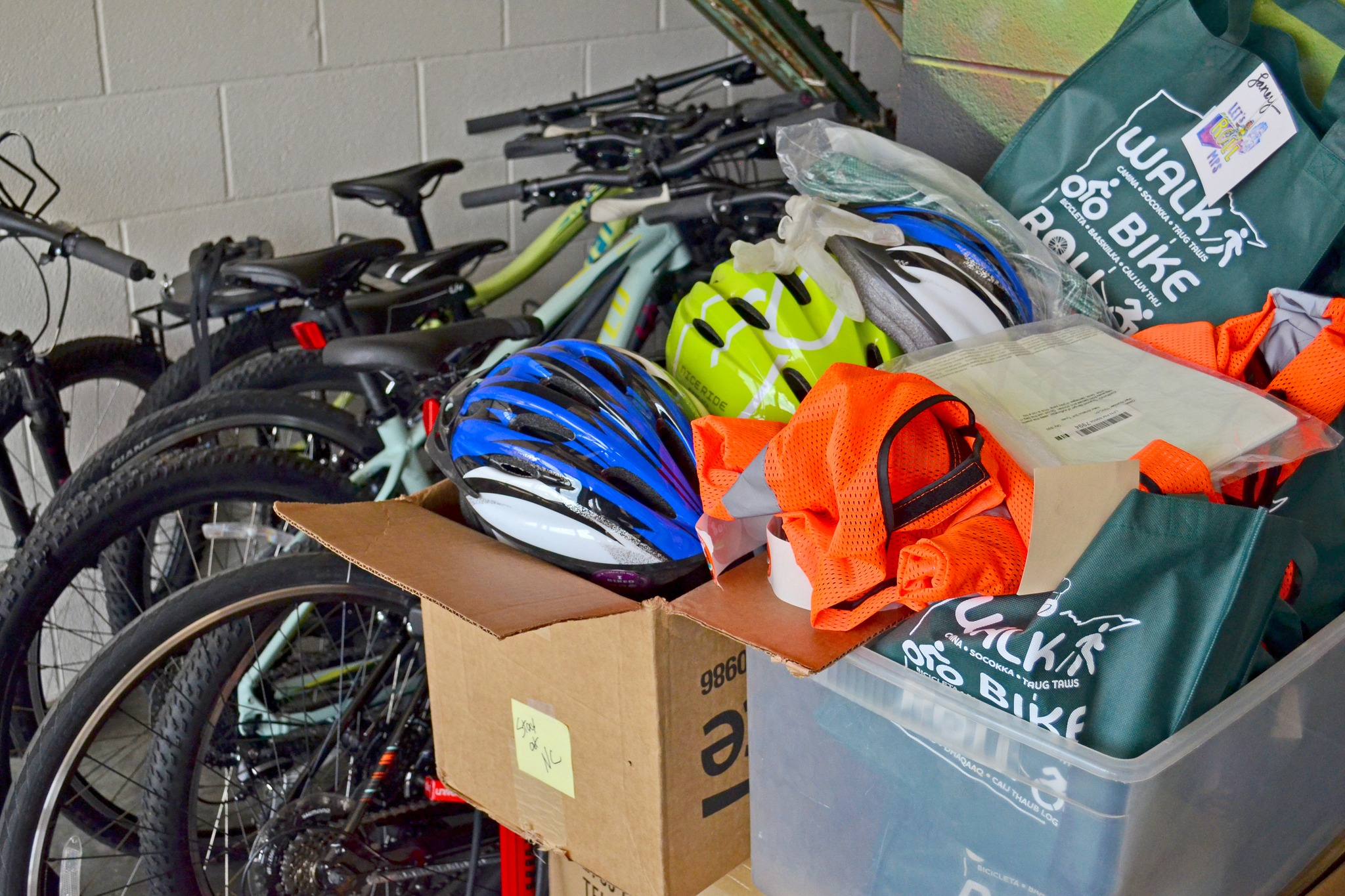 A box of high-visibility vests and helmets sit in front of a collection of bicycles. 