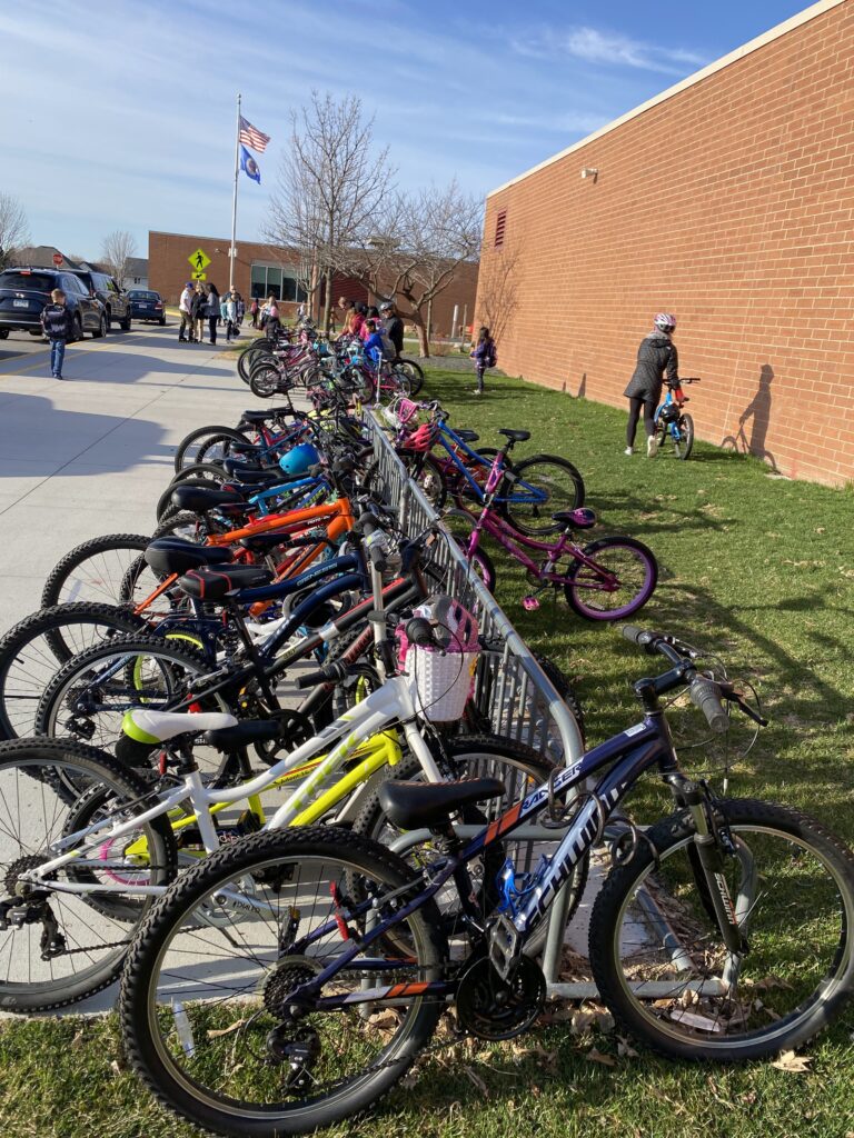 A bike rack is pictured full of bicycles with people in the distant background heading into a red-brick building